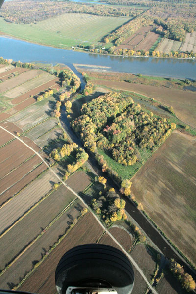 This aerial photograph shows a view of farmlands and a few small wooded areas along the Chicot River by Île Dupas.