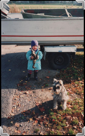 Girl holding a dead duck, in front of a boat.