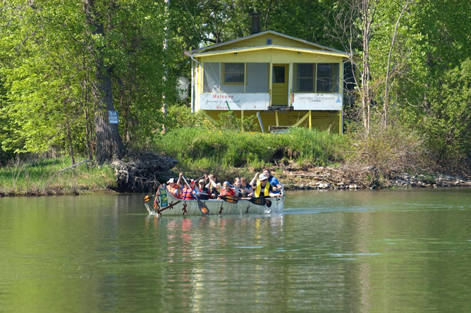 Several people paddle a Rabaska canoe along Chenal du Moine.