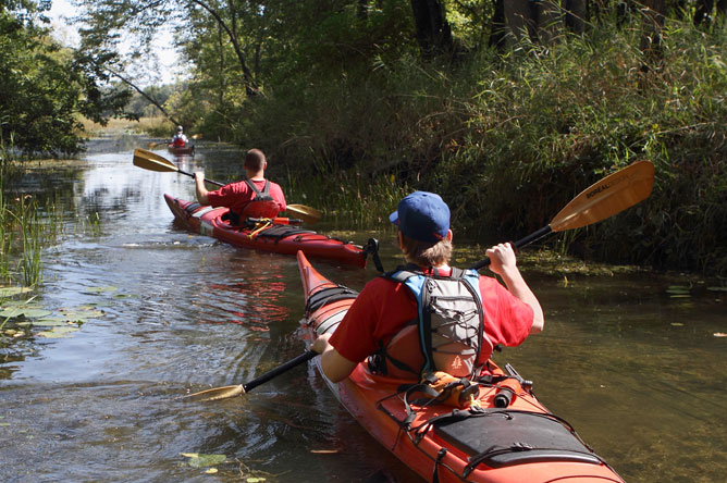 Trois jeunes kayakistes qui empruntent un chenal très étroit envahi par les plantes.