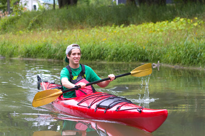 Front view of a young man paddling a red kayak along a channel.