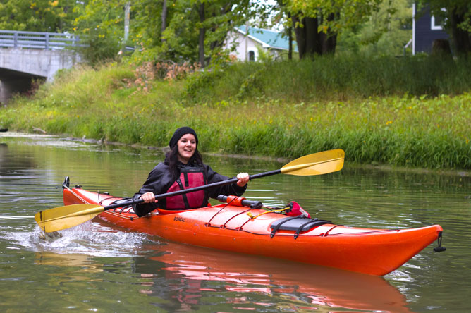 A woman paddles a red kayak along a channel.