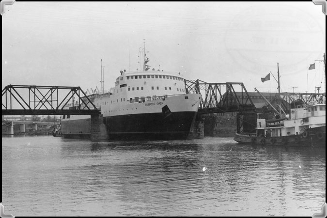 The ferry 'Ambrose Shea' sailing between the pillars of a railroad bridge over the Richelieu.