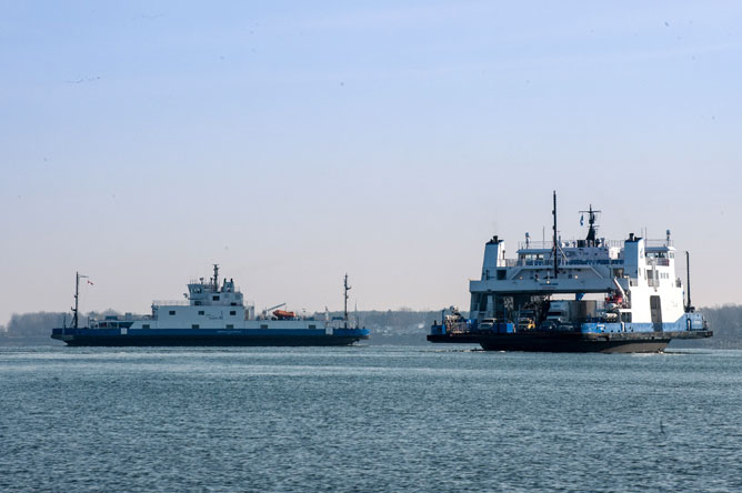 On voit deux traversiers naviguant sur le fleuve Saint-Laurent et en arrière-plan une île.