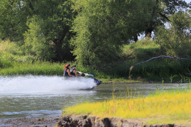 A woman and a man ride a personal watercraft along a channel.