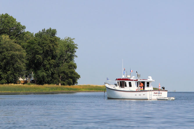 A man aboard a white and red pleasure craft moored in a channel.