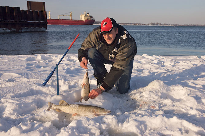 Un homme montrant les deux brochets qu'il a pêchés en hiver.