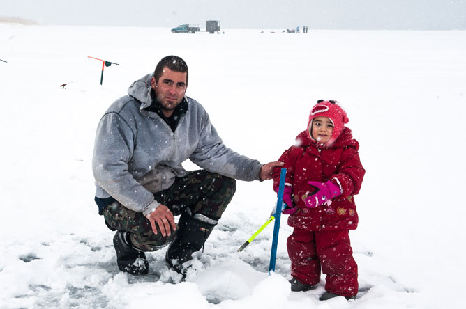 Young girl ice fishing with her father.
