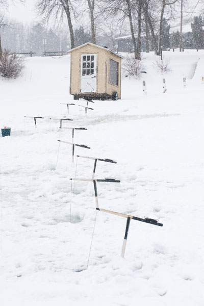 Ten tip-ups set up in front of a fishing cabin on the ice.