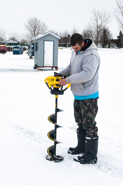 A fisherman bores a hole through the ice.