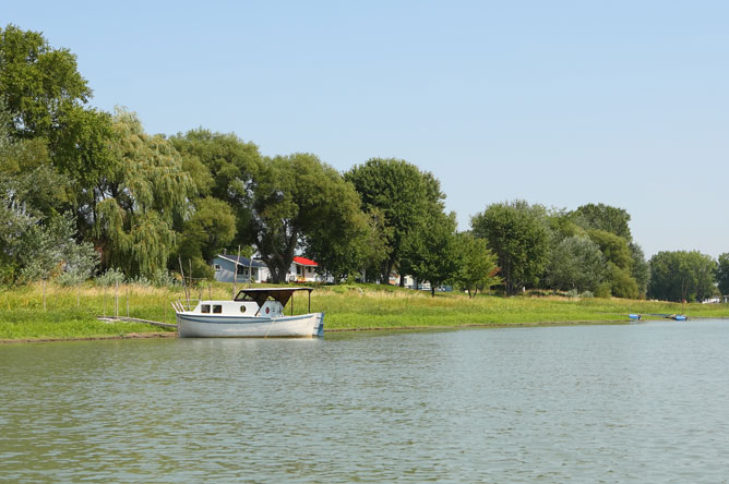 Small white boat moored alongside a dock on an island with several cabins.