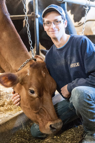 Young farmer holding the head of a light brown cow.