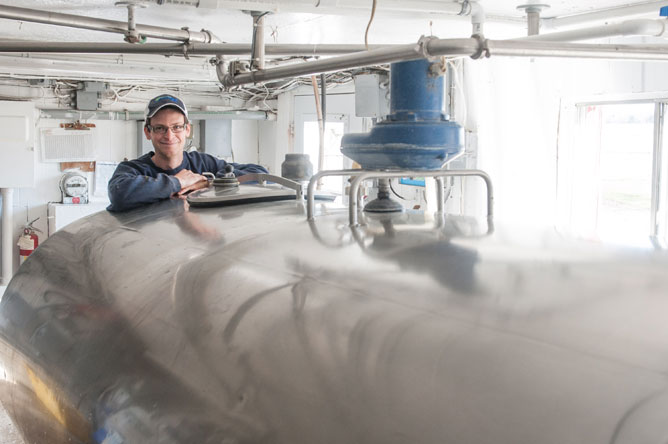 Young farmer presenting the bulk milk cooling tank that contains his cows' milk production.