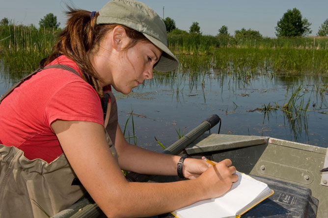 Une femme, à bord d'une chaloupe, écrivant dans un cahier.