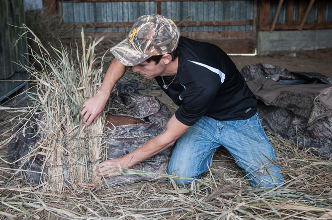 A young man covers a blind in dry vegetation.