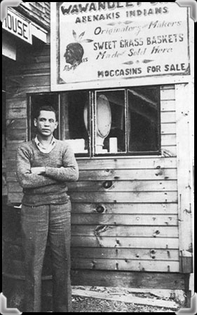 A man in front of his counter of Abenaki baskets and souvenirs, circa 1931