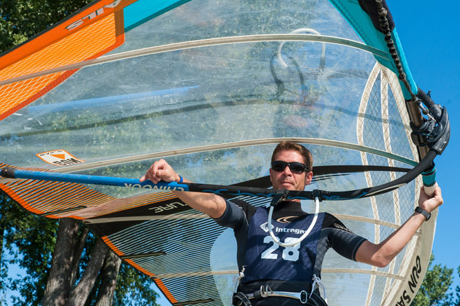 Un homme transportant une voile, transparente, orange et turquoise, au-dessus de lui.