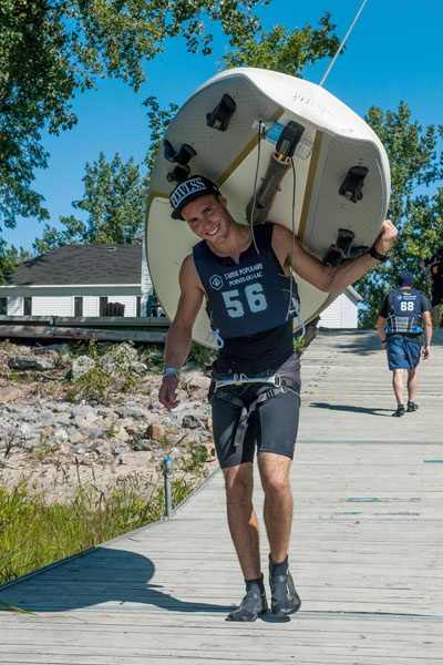 Man carrying a sailboard on his back.