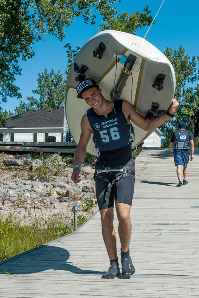 Un homme transportant sa planche à voile sur son dos.