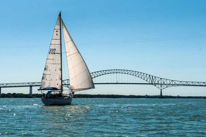 Un voilier blanc naviguant vers le pont Laviolette et deux navires commerciaux à l'horizon.