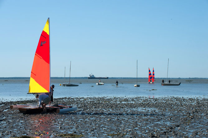 Several sailboats, including two with red and blue striped sails and one with a red, orange and yellow sail, and a commercial vessel on Lake Saint-Pierre