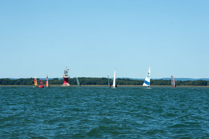 Plusieurs planches à voile multicolores sur le lac Saint-Pierre près d'un phare et d'une bouée rouges