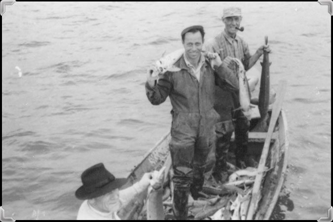 Three men in a small boat display the sturgeons they have landed.