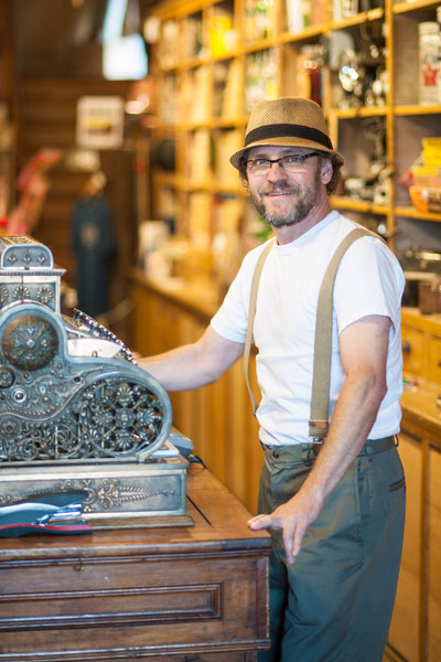 Homme vêtu à l'ancienne devant la caisse enregistreuse à l'intérieur du Magasin général Le Brun