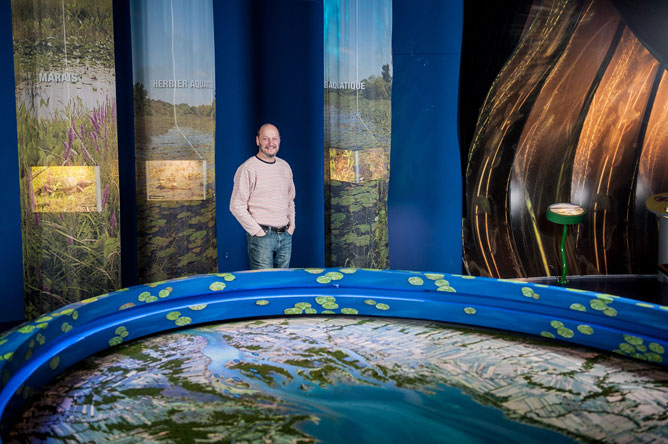 Un homme debout derrière une grande maquette montrant la région du lac Saint-Pierre.